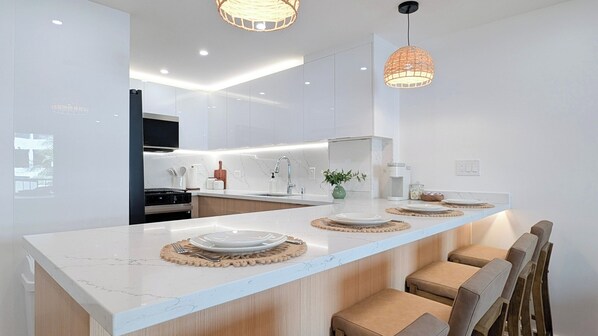 Cocina moderna con una isla central, encimeras de mármol blanco e iluminación colgante.