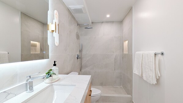 Un baño moderno con un espejo grande, un lavamanos con una planta, un inodoro y una zona de ducha.
