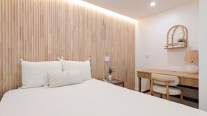 A bedroom with a wooden slat wall, a bed with white bedding, a bedside table with a lamp, and a desk with a chair.
