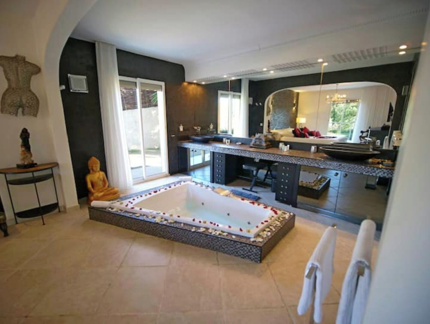 A modern bathroom with a large bathtub, a sitting area, and a mirror.