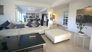 Un salon moderne avec un canapé, une table basse noire et un pouf blanc. Une plante en pot est posée sur une table d’appoint.