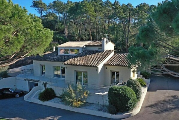 Une maison à deux étages, avec un toit en tuiles, entourée d’arbres et dotée d’une allée.