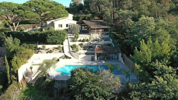 Une grande maison avec une piscine, entourée d’arbres et de verdure luxuriante.