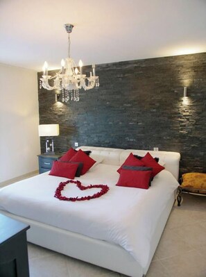 Une chambre à coucher avec un grand lit, un lustre, un mur décoratif en pierre et une lampe de chevet.