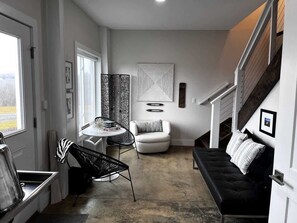 Una sala de estar moderna con un sofá negro, un sillón blanco, una mesa de comedor con sillas y una escalera.