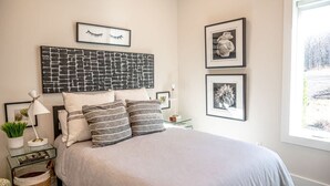 A neatly arranged bedroom with a bed, bedside tables, and framed artwork on the walls. - The Gathering Barn by Buffalo Mountain Getaway (Meadows of Dan)
