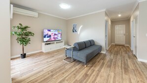 A modern living room with a grey sofa, a flat-screen TV, a small side table, a potted plant, and a wooden floor. - Modern 4X2 Perth house near Stadium/Casino/Airport (Cloverdale)
