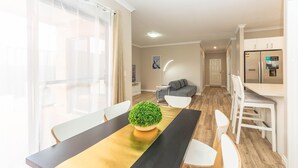 A modern dining area with a long table, white chairs, and a potted plant. - Modern 4X2 Perth house near Stadium/Casino/Airport (Cloverdale)