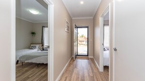 A hallway with a wooden floor leading to a bedroom with a bed and a window. - Modern 4X2 Perth house near Stadium/Casino/Airport (Cloverdale)