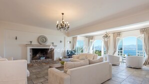 A spacious living room with a fireplace, comfortable seating, and large windows offering a scenic view. - Villa with enormous Pool in Kassiopi (Kassiopi)