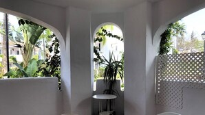 Uma área de refeições com uma mesa e cadeiras, uma pequena mesa redonda com um vaso de planta e um painel treliçado.