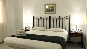 Uma cama bem arrumada com cabeceira preta, duas mesas de cabeceira com abajures, e um quadro na parede.
