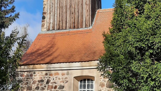 Un bâtiment rustique en pierre, doté d’une tour en bois et d’un toit recouvert de tuiles rouges.