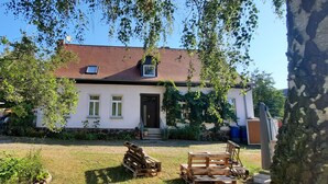 Une maison avec un toit rouge, des murs blancs et une porte d’entrée. Il y a une petite fenêtre au deuxième étage et une antenne parabolique sur le toit.