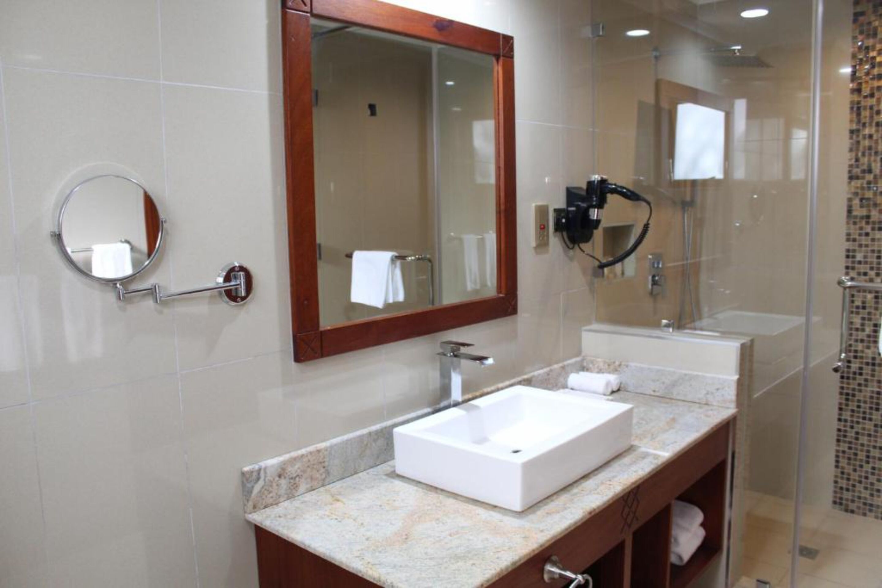 A modern bathroom with a large mirror, two sinks, and a shower area.