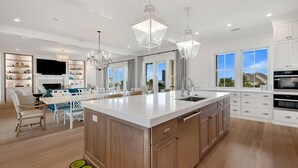 A spacious kitchen with a large island, white cabinetry, and pendant lighting.