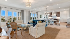 A spacious living room with a blue sofa, striped armchairs, and a dining area with white chairs.
