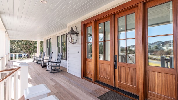 A covered porch with wooden flooring, rocking chairs, and a large wooden door with glass panels.