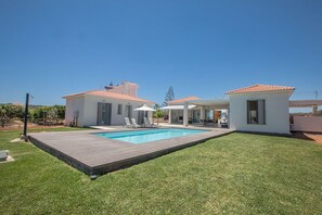 Una casa moderna con piscina, patio y césped bien cuidado.