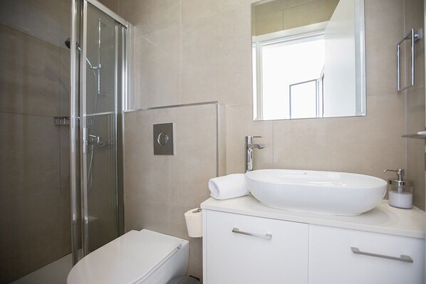 A modern bathroom with a glass shower enclosure, a white sink, and a toilet.