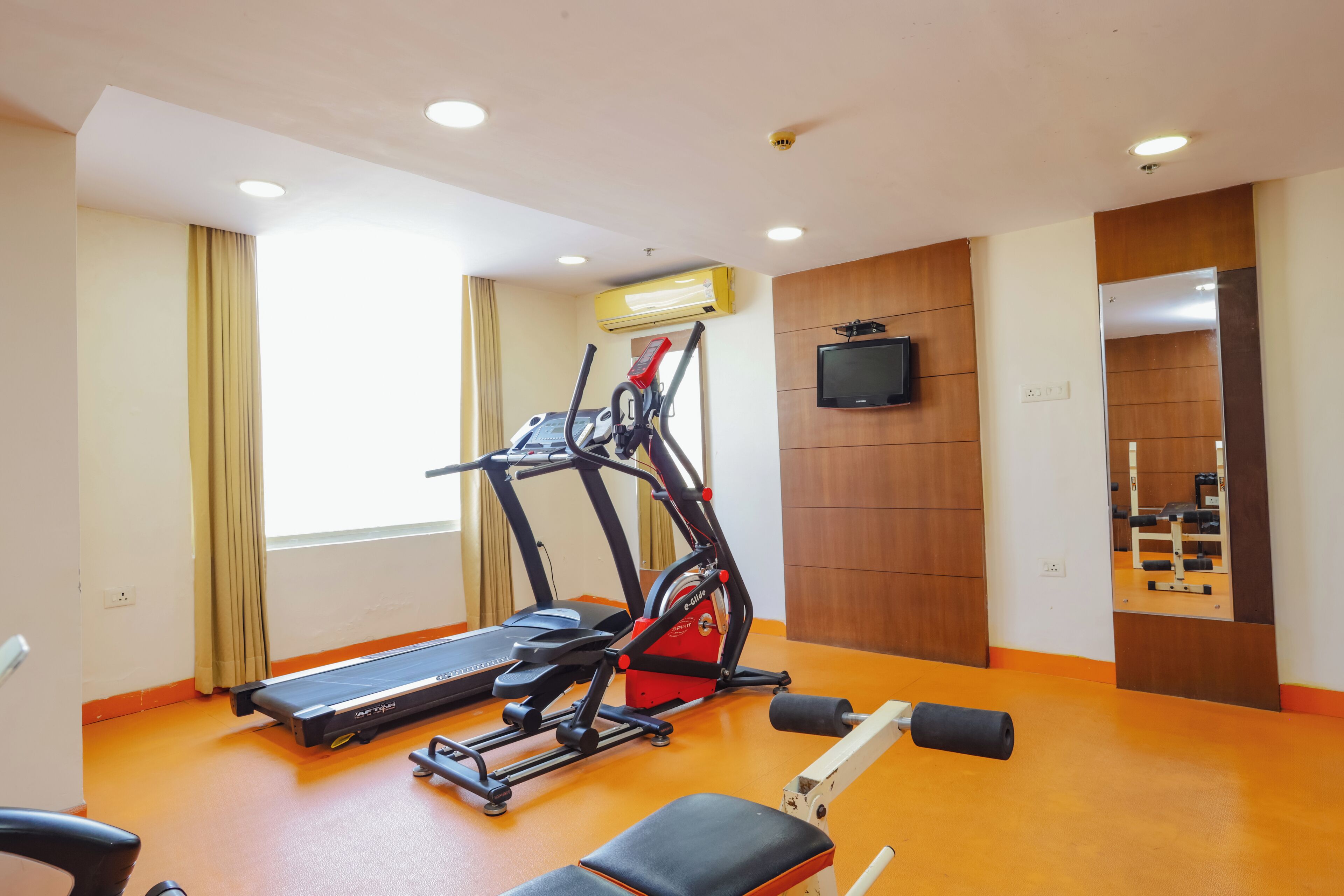 Un gimnasio con equipo de ejercicio, cinta de correr, bicicleta estática y banco para pesas.
