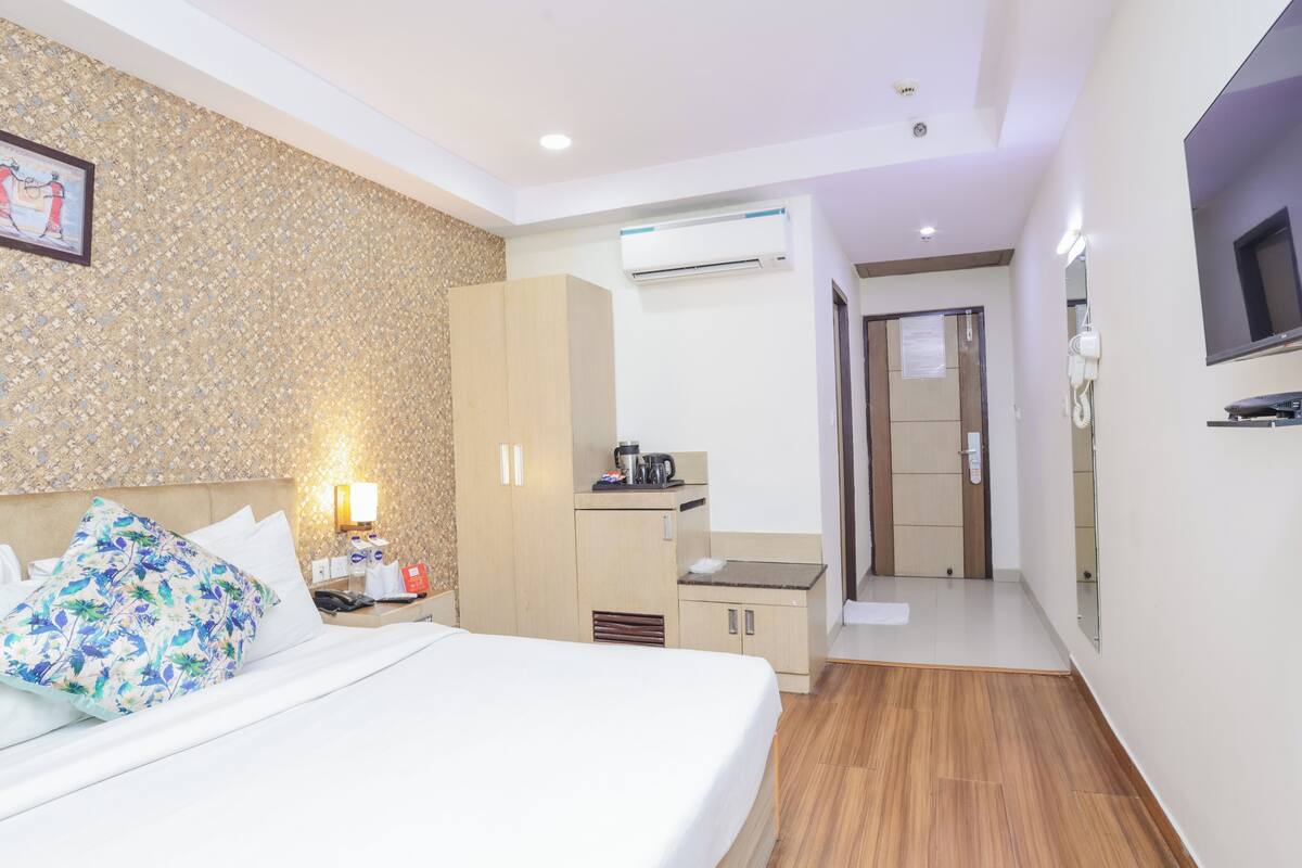 A hotel room with a bed, a nightstand, a wardrobe, a small kitchenette, and a bathroom.