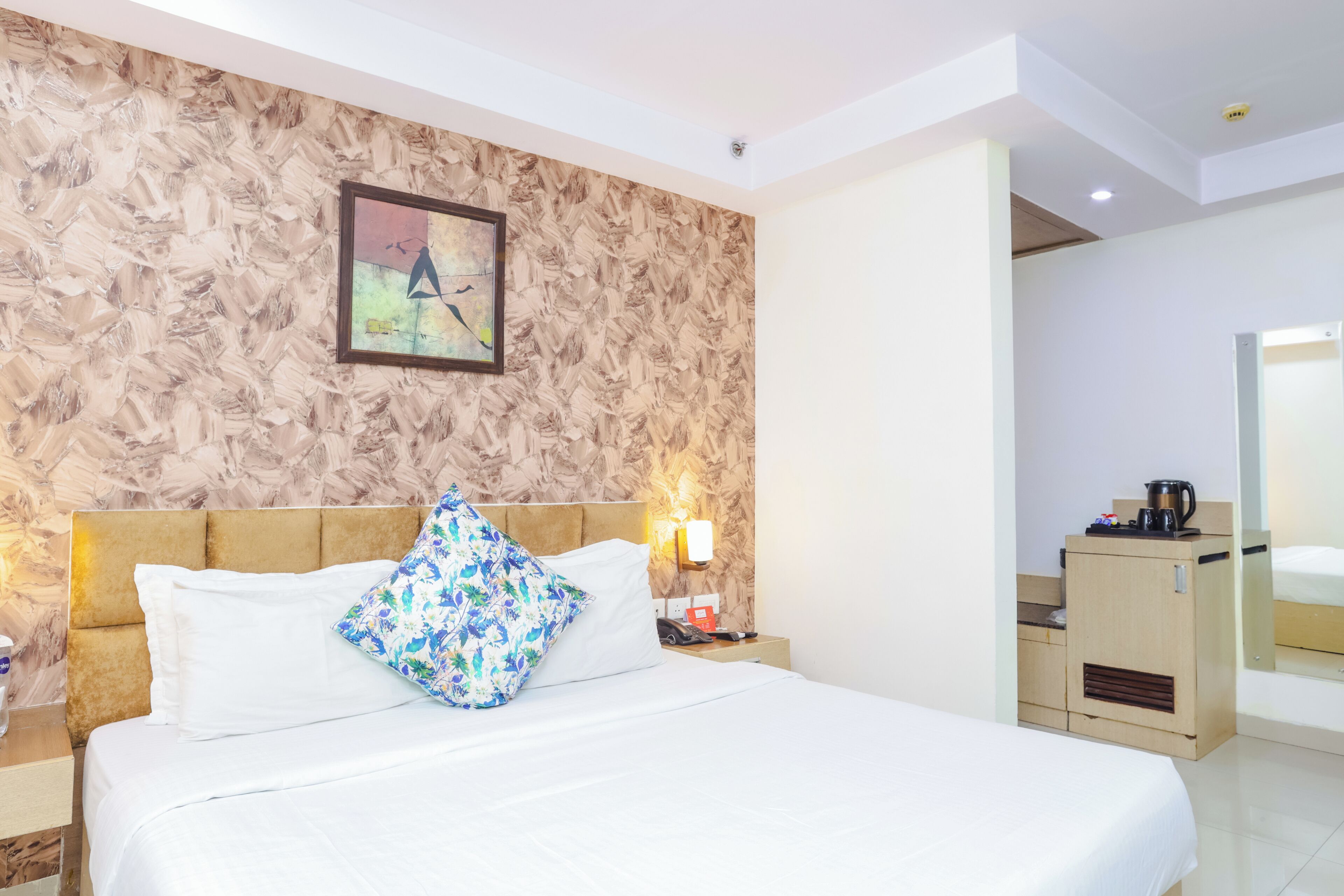 Ein Hotelzimmer mit einem Bett, einem Nachttisch, einem Wandbild und einer kleinen Küchenzeile.