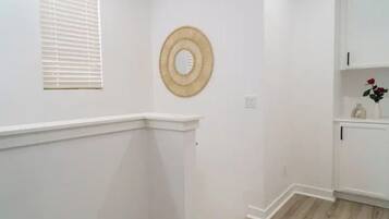 A hallway with white walls, a wooden floor, a white door, and a small shelf with a vase and a rose.