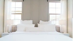 A modern hotel room with a large bed, two bedside tables, and a window with curtains.