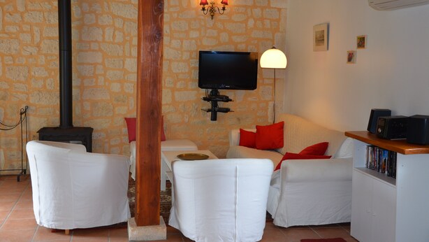 A cozy living room with stone walls, a fireplace, white furniture, a TV, and a bookshelf. - Air-conditioned, garden, private heated pool, pets welcome.  (Eyraud-Crempse-Maurens)