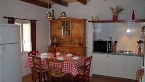 A dining area with a wooden table and chairs, a kitchen with cabinets and appliances, and a window with curtains. - Air-conditioned, garden, private heated pool, pets welcome.  (Eyraud-Crempse-Maurens)