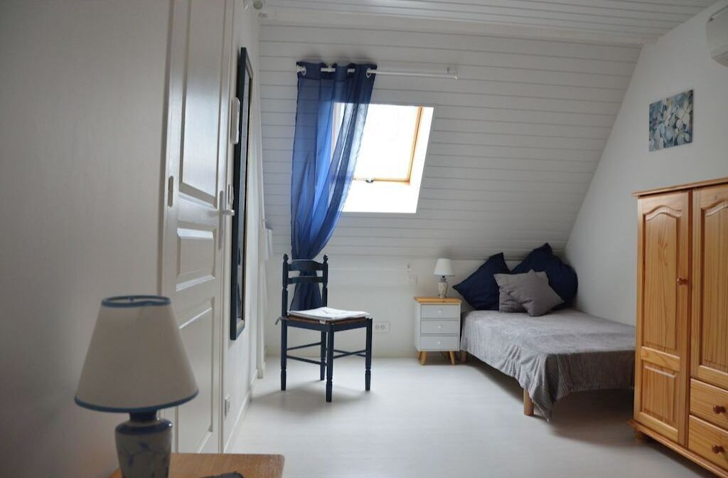 Une chambre à coucher comprenant un lit, une chaise, une table de chevet, une lampe, une armoire et une fenêtre avec des rideaux bleus.