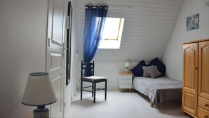 Une chambre à coucher comprenant un lit, une chaise, une table de chevet, une lampe, une armoire et une fenêtre avec des rideaux bleus.