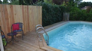 Une terrasse en bois avec une piscine, une chaise et une petite table.