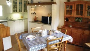 Un coin repas avec une nappe à rayures, des chaises en bois et une cuisine en arrière-plan.