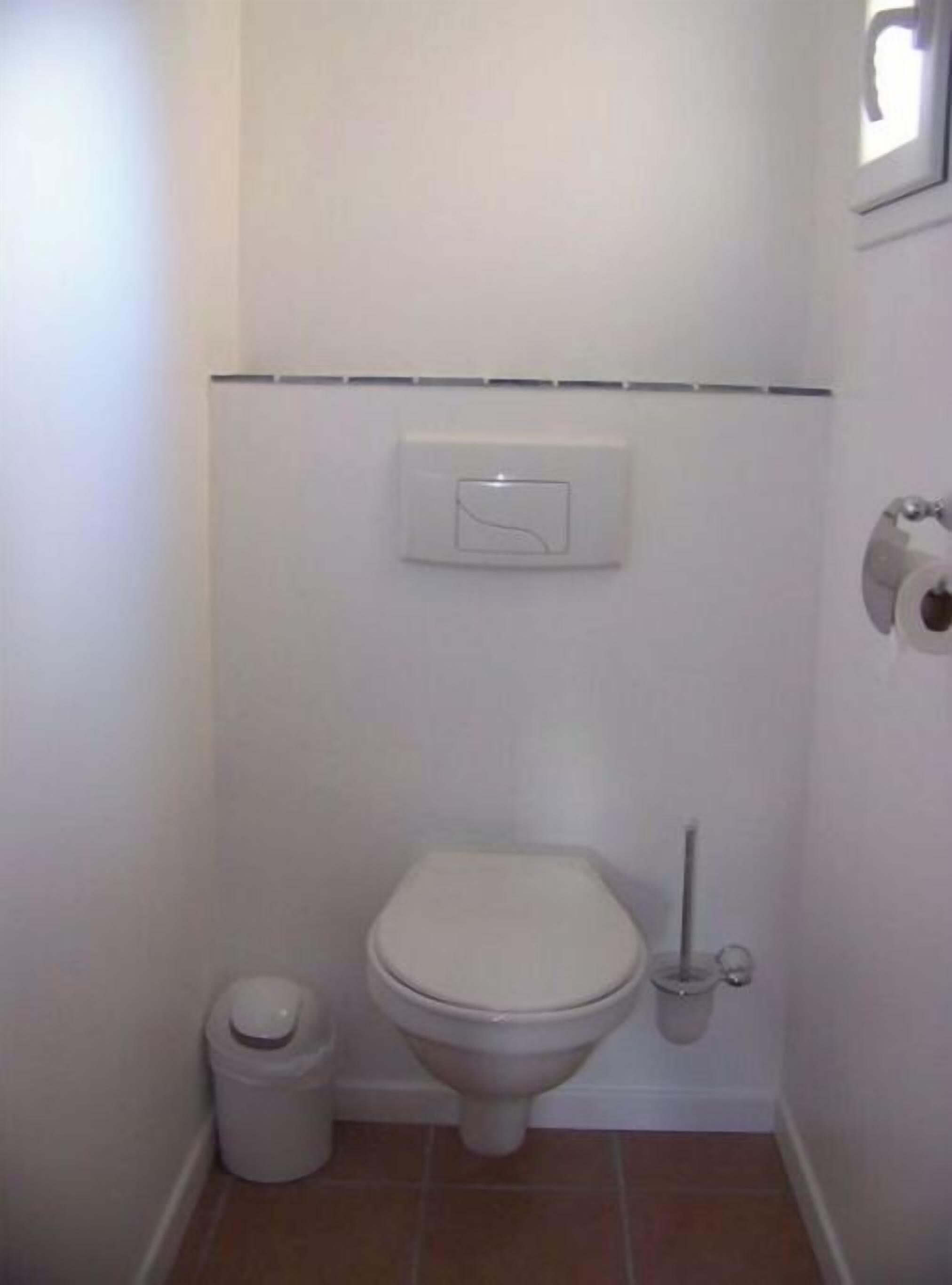 A small, white bathroom with a toilet, a trash can, and a toilet paper holder.