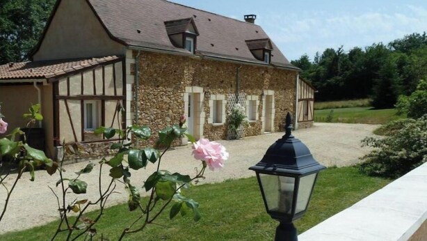 Une maison en pierre avec un toit en tuiles, une allée en gravier et une fleur au premier plan.