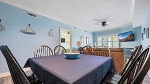 A dining area with a table set for four, chairs, a ceiling fan, and a window with blinds. - Three bedroom condo with large side balcony allows for viewing of sunrises & sunset (Ocean City)