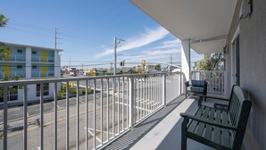 A balcony with a view of a street, a bench, and a building with a yellow door. - Three bedroom condo with large side balcony allows for viewing of sunrises & sunset (Ocean City)