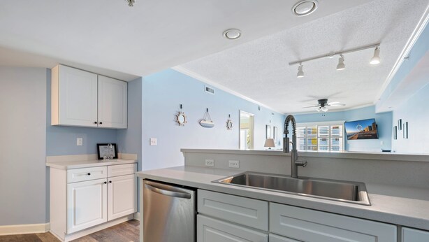 A modern kitchen with white cabinetry, a stainless steel dishwasher, and a built-in sink. - Three bedroom condo with large side balcony allows for viewing of sunrises & sunset (Ocean City)