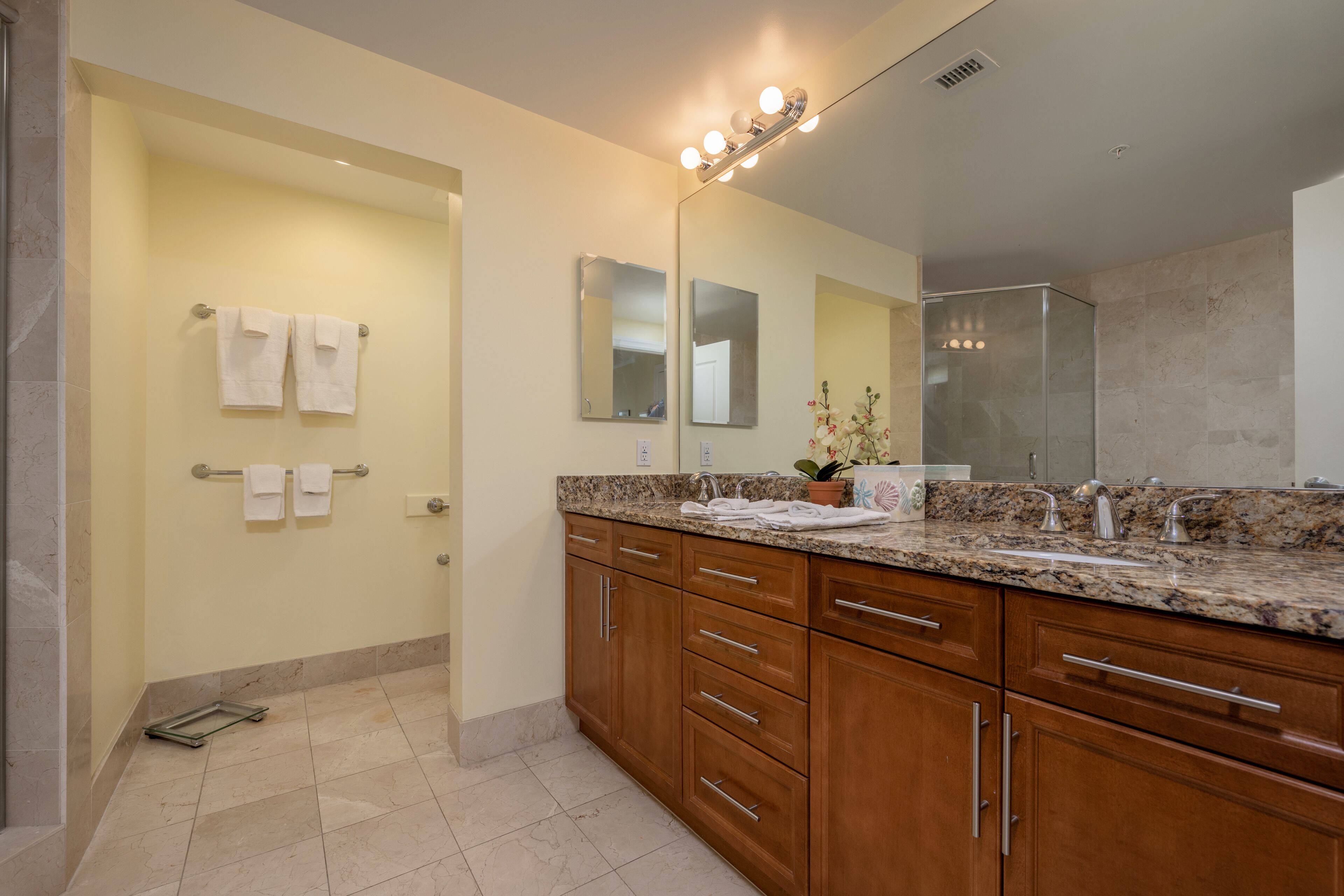 A modern bathroom with a marble countertop, wooden cabinets, a large mirror, and a shower area.