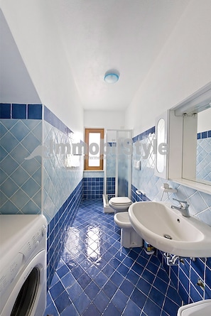 Un baño con azulejos azules, lavadora, lavamanos y espejo.