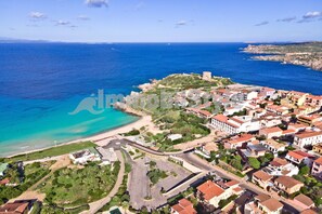 An aerial view of a coastal town with a mix of residential buildings, a prominent castle-like structure, and a beach area.