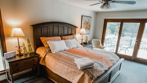 Een slaapkamer met een groot bed, twee nachtkastjes, een plafondventilator en uitzicht op de omgeving via een schuifdeur.'