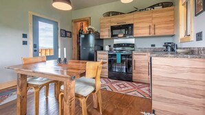 A modern kitchen with wooden cabinets, a dining table with chairs, and pendant lighting. - Teton Homestead: Ski Cabin w/ Teton Views (Driggs)