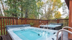 A hot tub area with two hot tubs, a wooden deck, and a wooden fence.