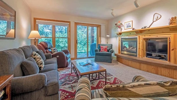 A cozy living room with a fireplace, comfortable seating, and large windows.