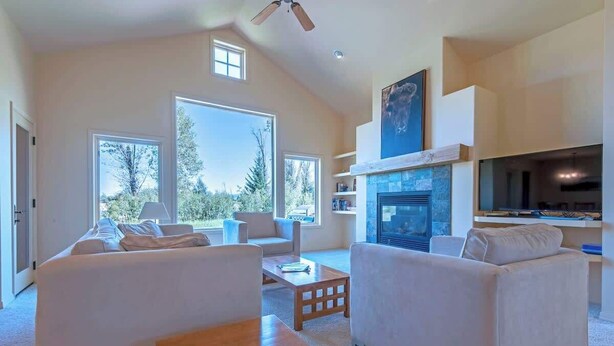 A spacious living room with a fireplace, large windows, and a ceiling fan. - Teton Homestead: Bunkbeds, Private Deck, Targhee (Driggs)