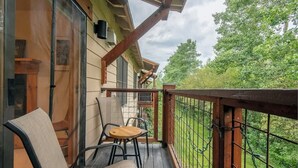 A wooden deck with a glass door leading to a room, a wooden table, and two chairs. - Teton Homestead: Modern Corner Top Unit + Hot Tub (Driggs)