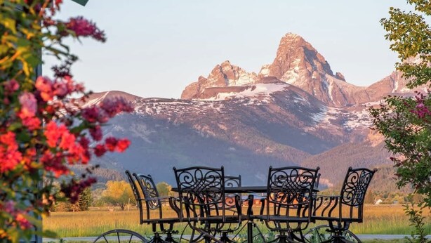A dining table with chairs in a scenic outdoor setting with mountains in the background. - Teton Homestead: Western Cabin w/ Hot Tub & Views (Driggs)